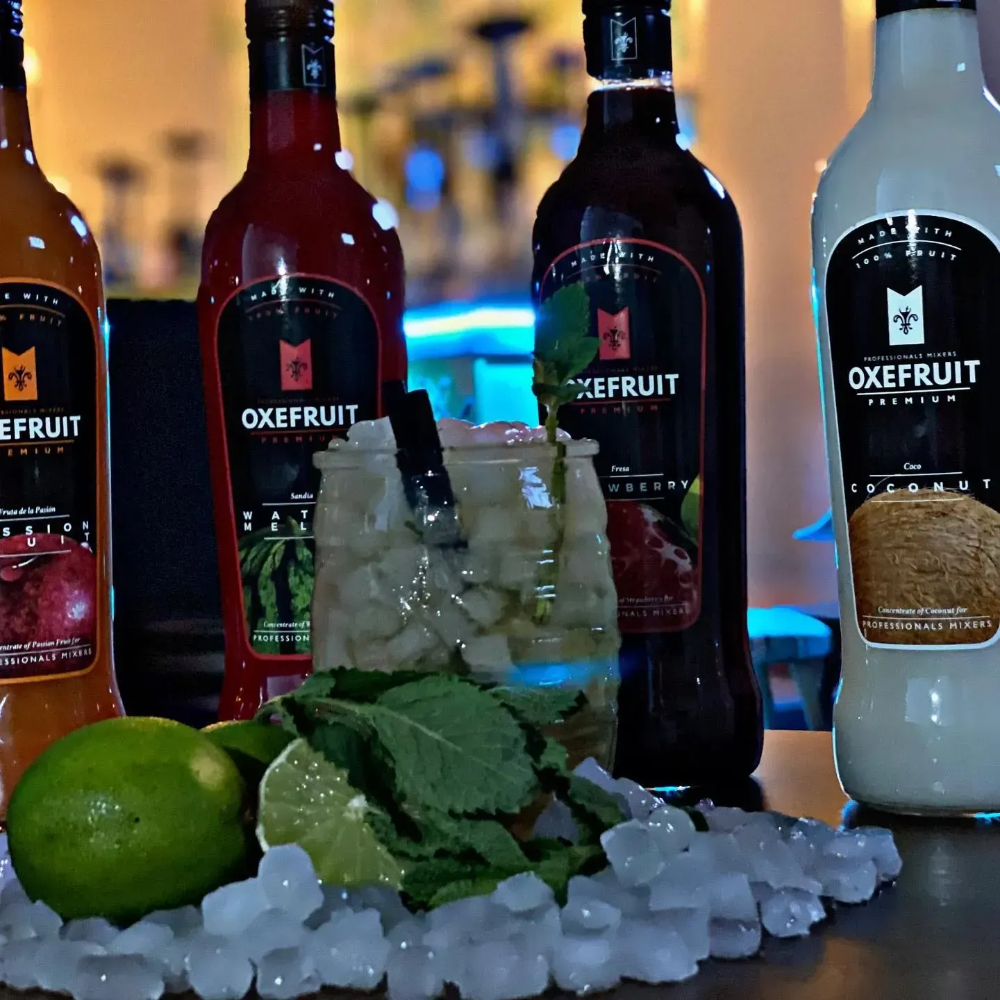 Botellas de mezcladores OxeFruit, con una bebida en el medio, rodeada de limas, menta y hielo.