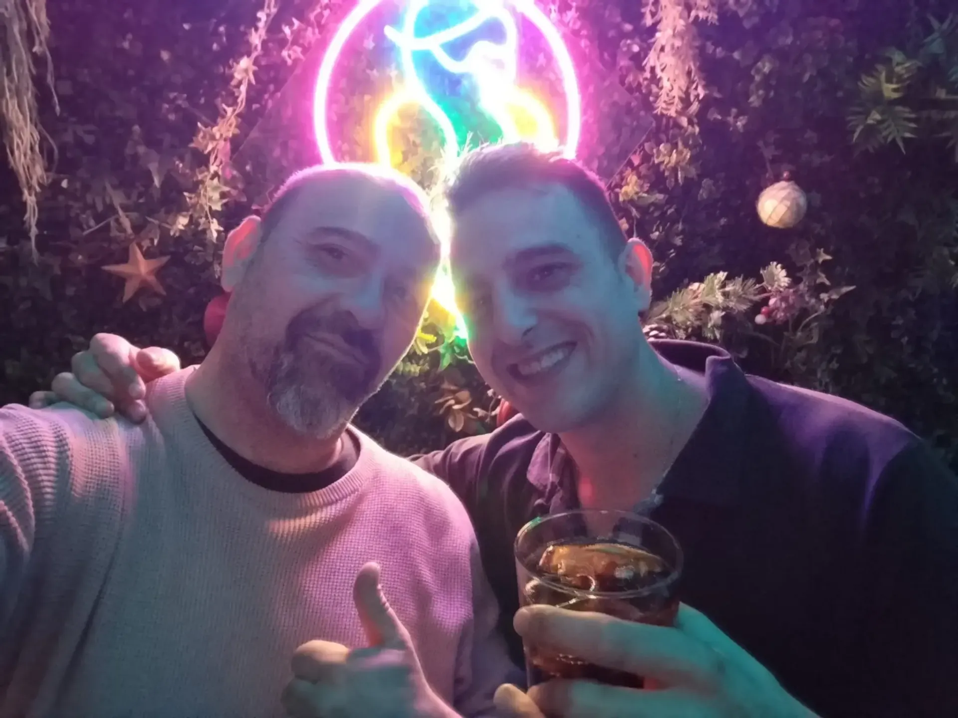 Dos hombres sonríen, posando juntos frente a un letrero.