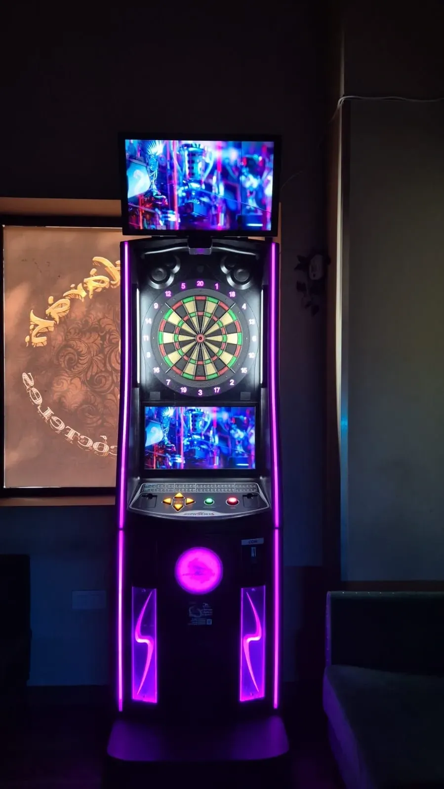 Máquina de dardos con luces de neón violeta, dos pantallas que muestran el juego y un tablero de dardos.