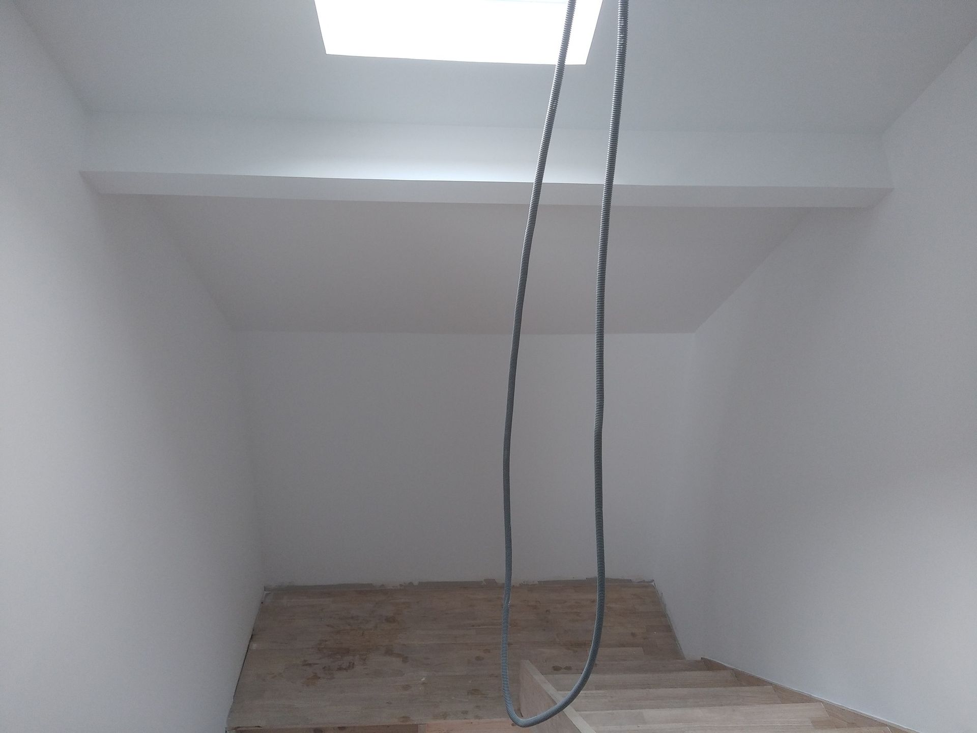 Pièce intérieure avec escalier menant à une plateforme. Une source lumineuse est placée au-dessus. Un câble pend.