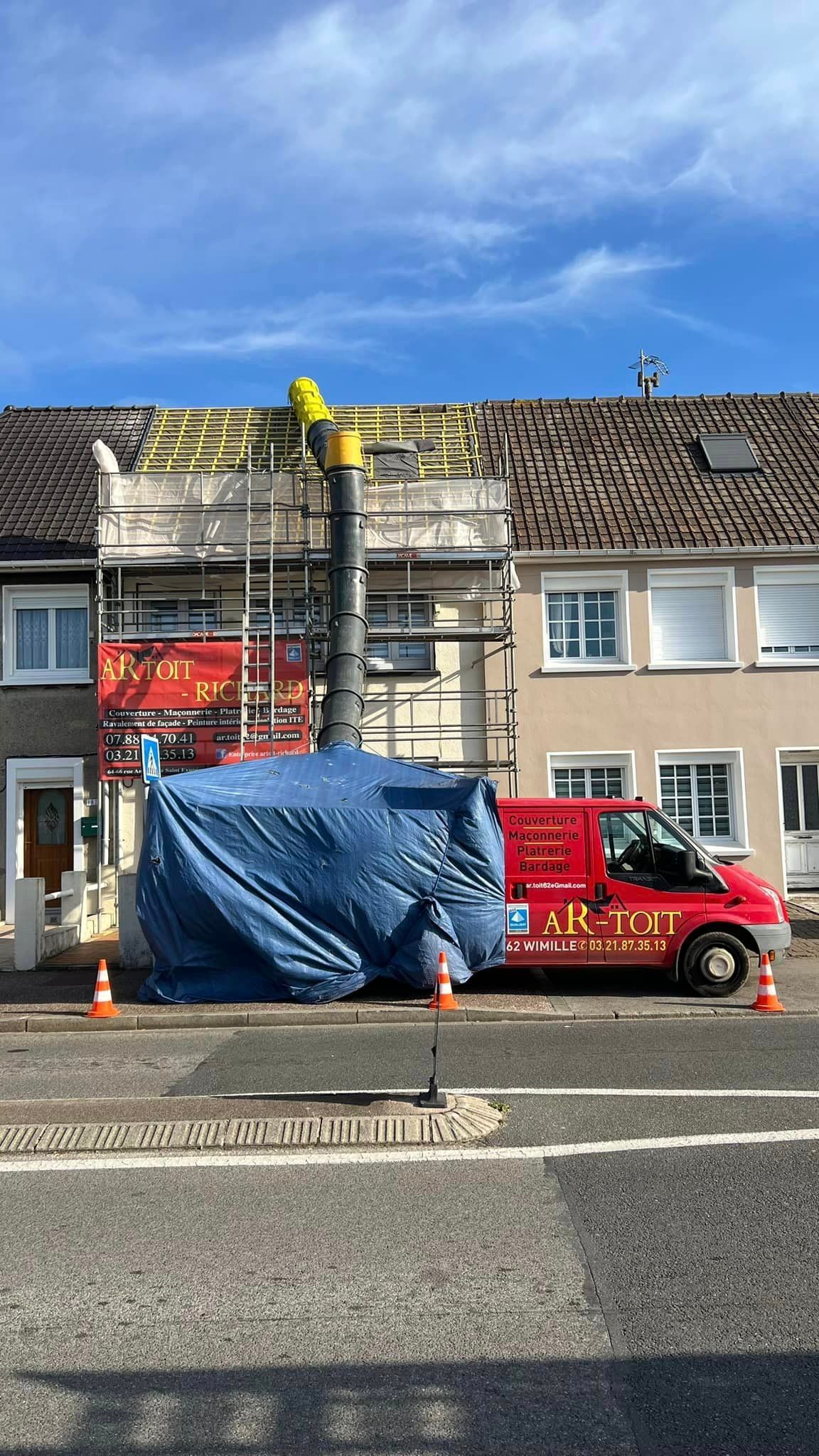 Travaux de construction sur une maison. Échafaudages, débris recouverts de bâches et camionnette rouge garée dans la rue.