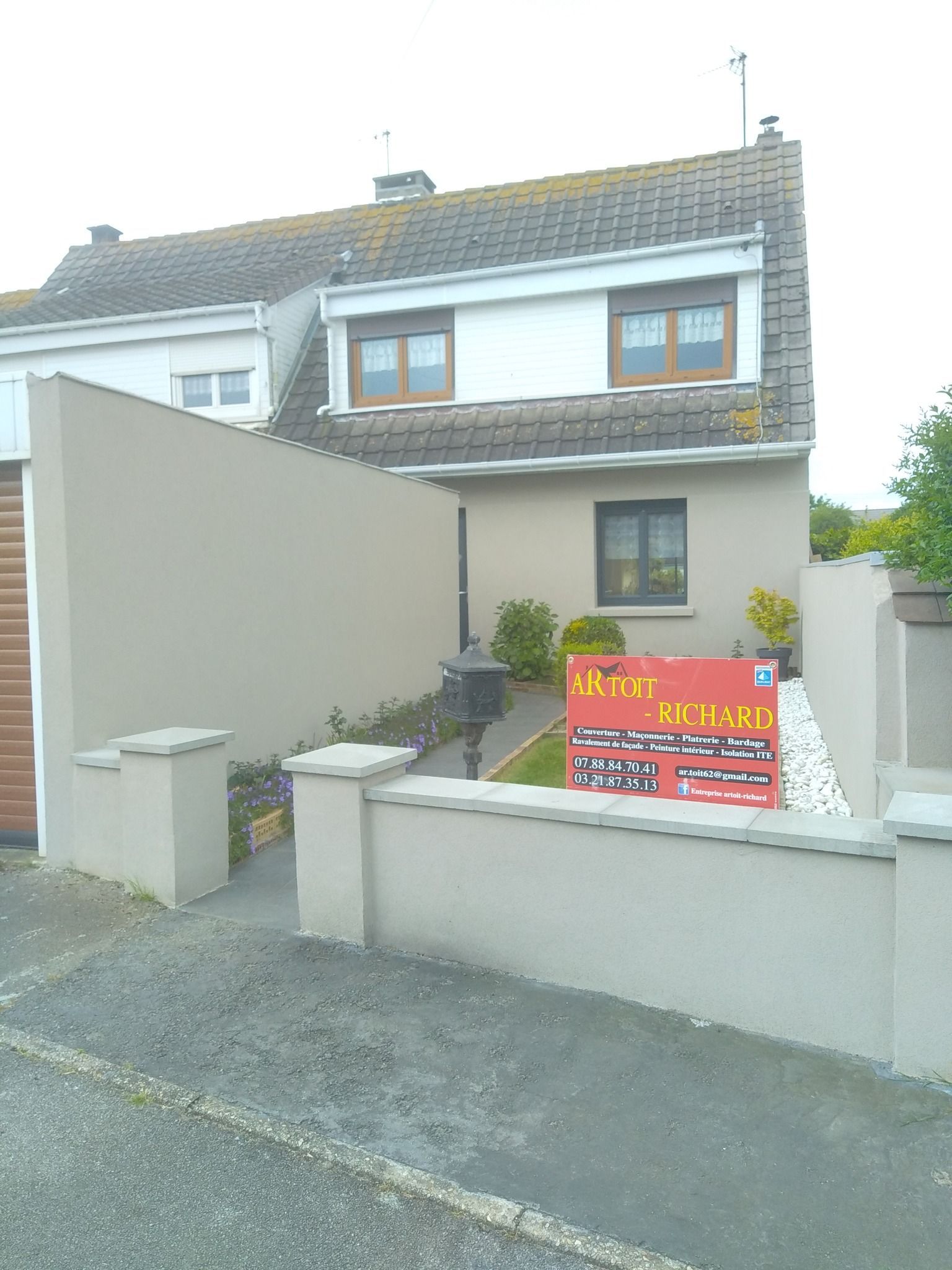 Maison à l'extérieur beige, murs couleur sable, allée et panneau.