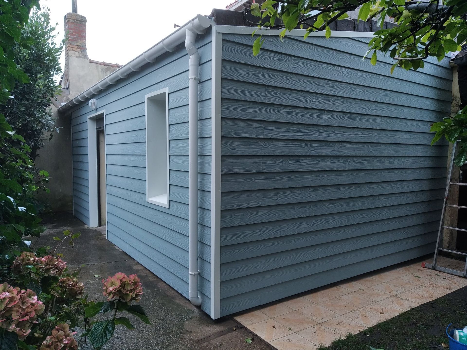 Petite maison avec bardage bleue, une porte et une fenêtre.