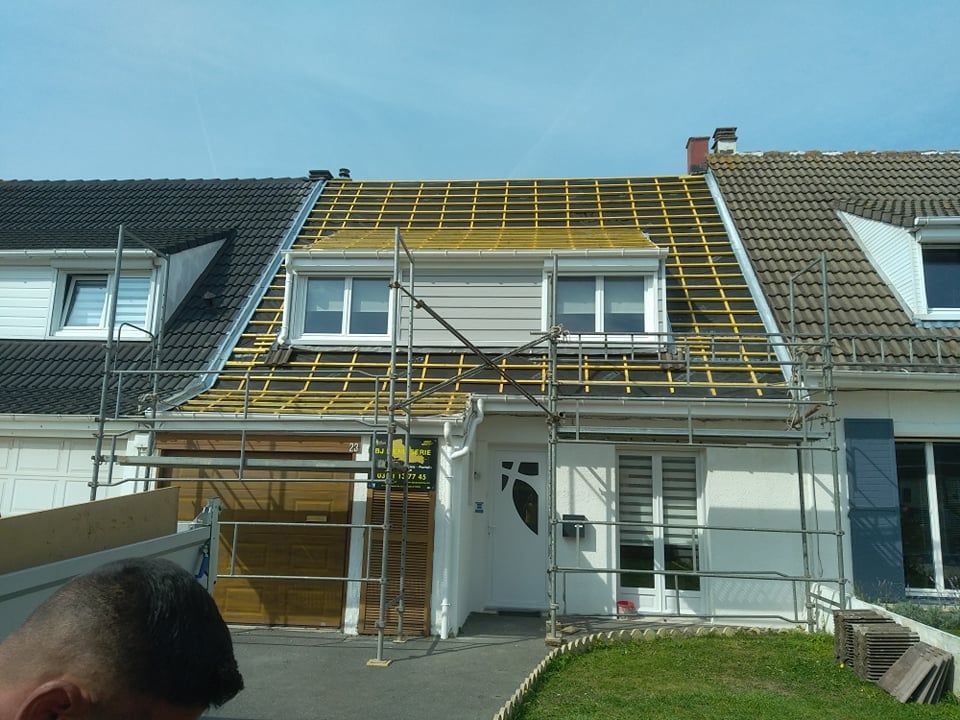 Maison en construction ; charpente apparente, échafaudages, bardage blanc.