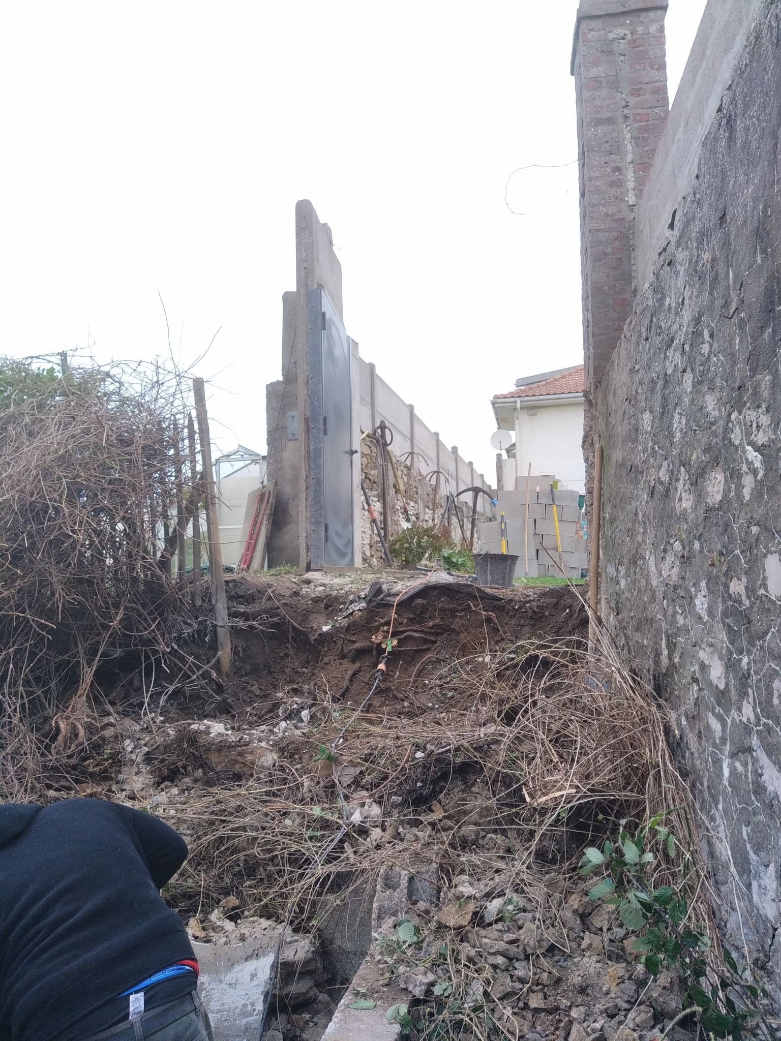 Une personne près d'un tas de débris, à côté d'un haut mur de béton et d'une structure partiellement détruite.