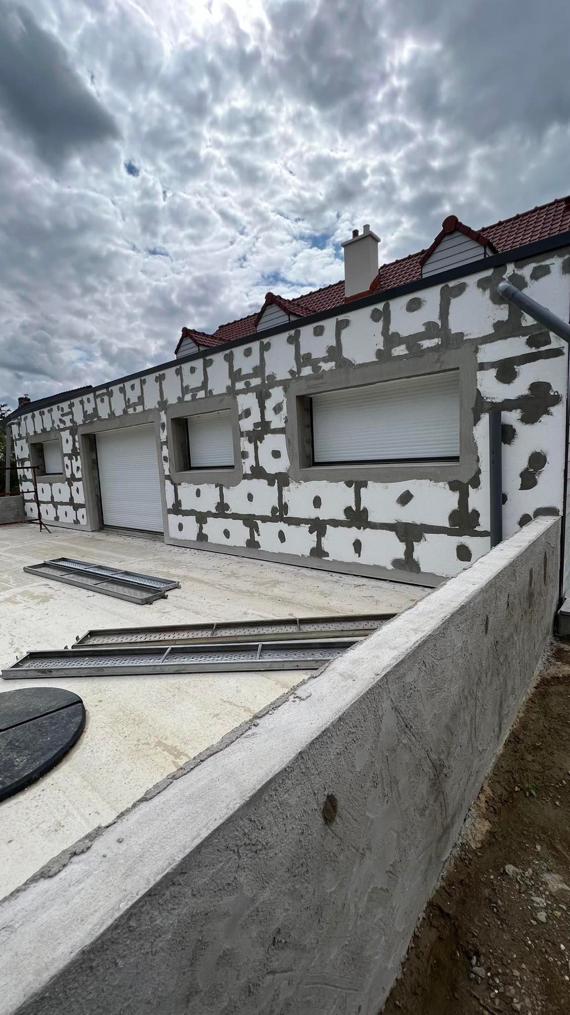 Extérieur d'un bâtiment en construction, isolation en mousse blanche appliquée sur les murs, ciel couvert.