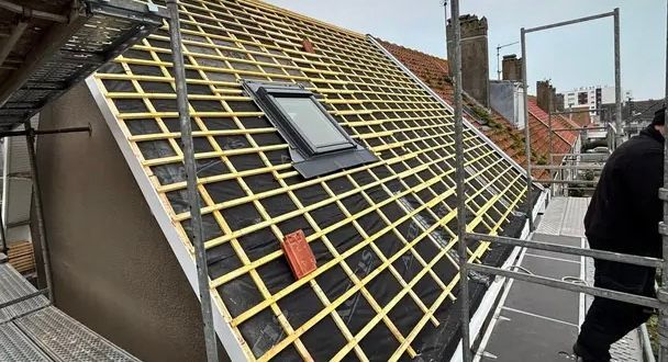 Toiture en construction ; poutres en bois et membrane noire visibles. Puits de lumière installé. Échafaudages présents.