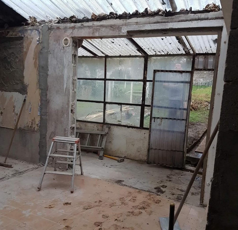 Intérieur d'un bâtiment délabré avec une porte et des fenêtres à panneaux de verre. Des matériaux de construction sont éparpillés.