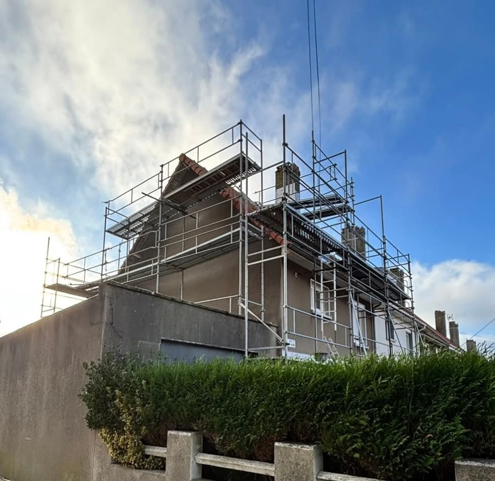 Des échafaudages entourent une maison en travaux de toiture, sous un ciel nuageux.