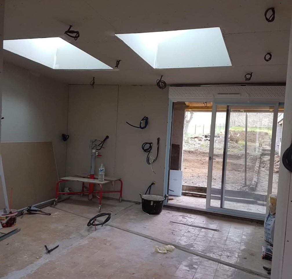 Pièce en construction avec puits de lumière et porte coulissante, câblage électrique apparent.