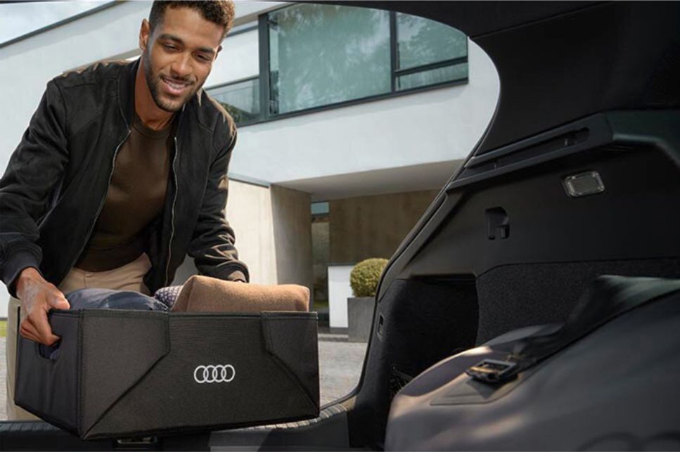 Blick durch den Innenraum eines Autos beidem ein Mann eine Box in den Kofferraum stellt.