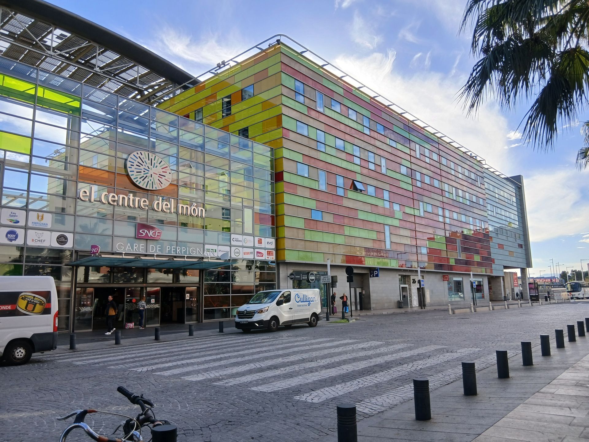 Bâtiment coloré El Centre de Mar avec façade en verre et passage piéton ; journée ensoleillée.