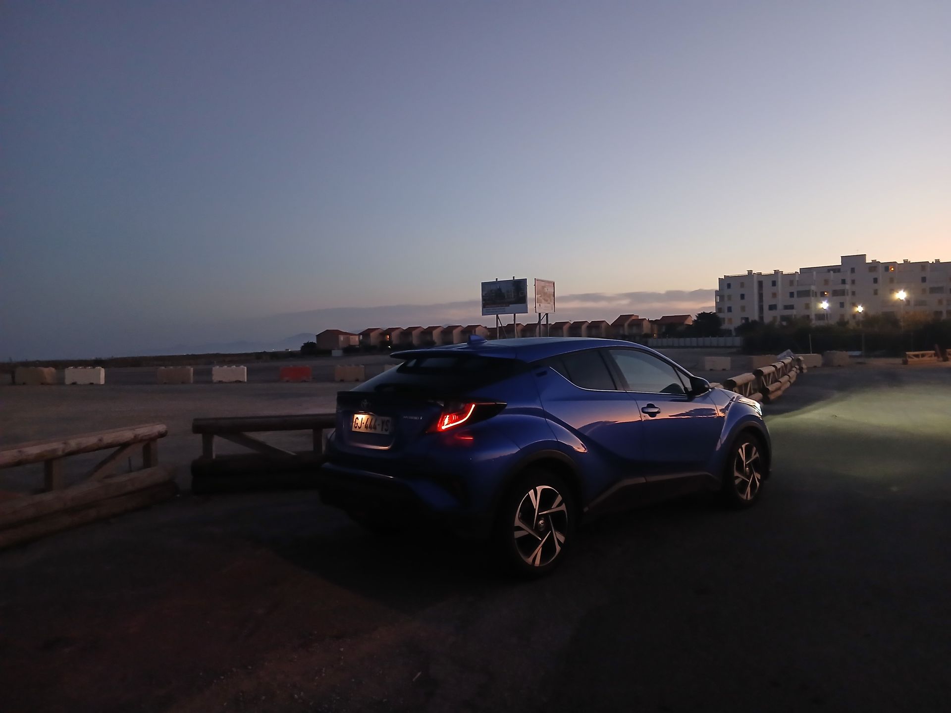 Une Toyota C-HR bleue est garée près d'un point d'eau au crépuscule, sous un ciel qui s'assombrit.