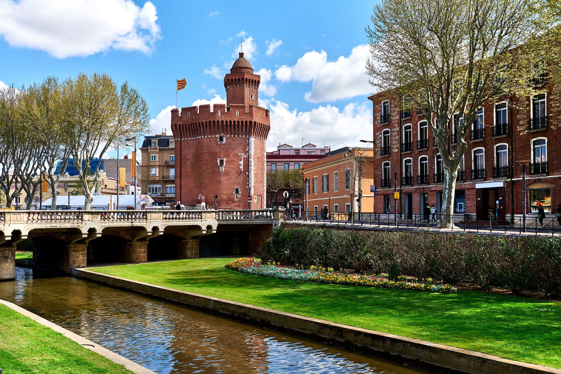 Tour en briques et pont enjambant un canal dans une ville européenne, journée ensoleillée sous un ciel bleu.
