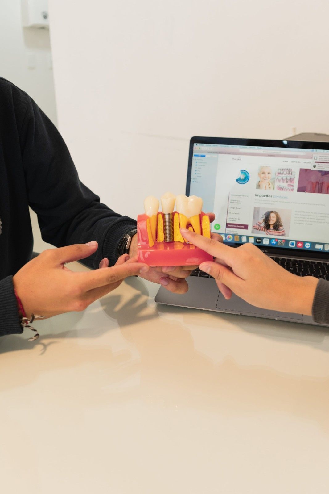 Dos personas sostienen un modelo dental de dientes con un puente, con una computadora portátil