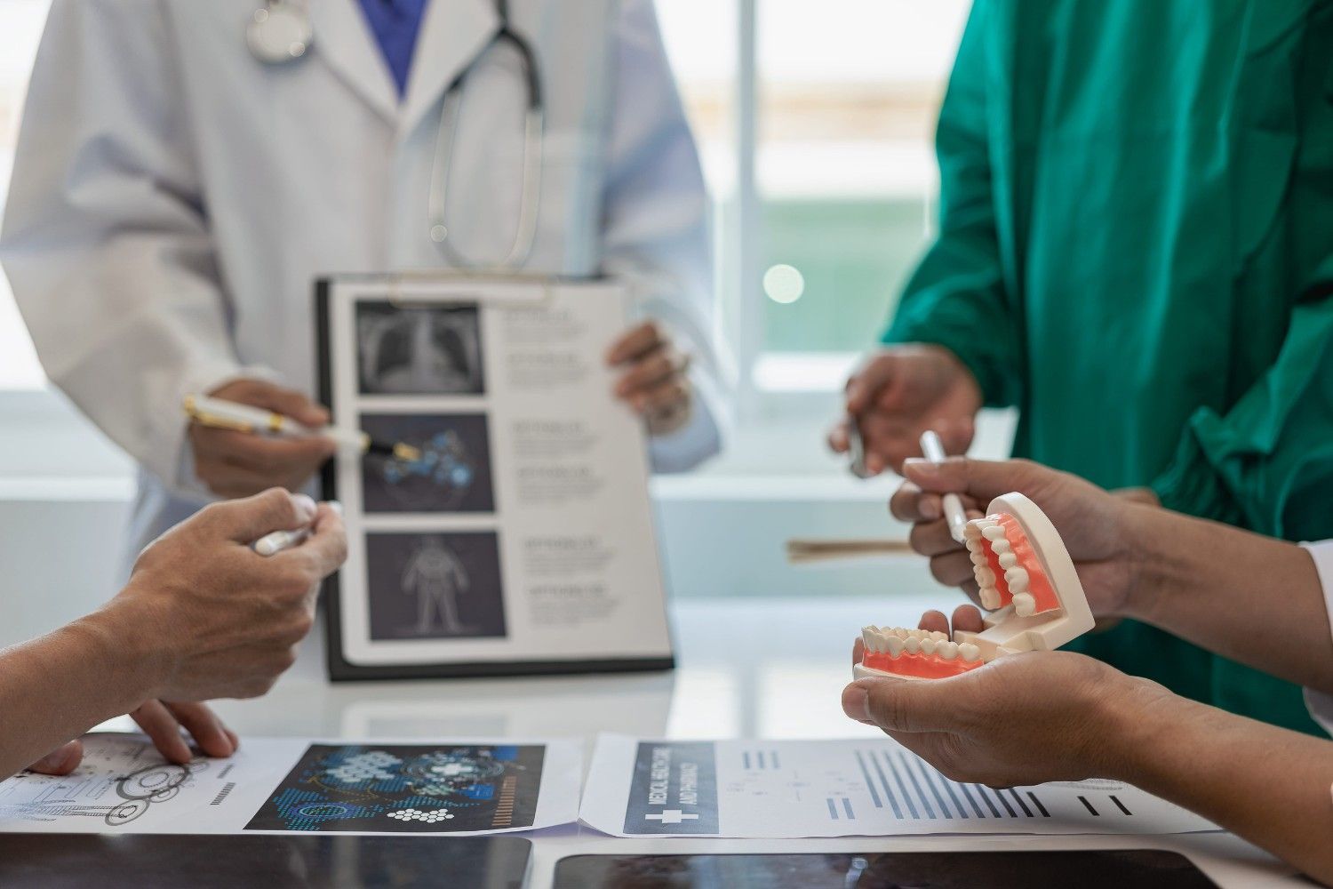 En un entorno clínico, profesionales médicos revisan radiografías y un modelo dental durante una consulta colaborativa.