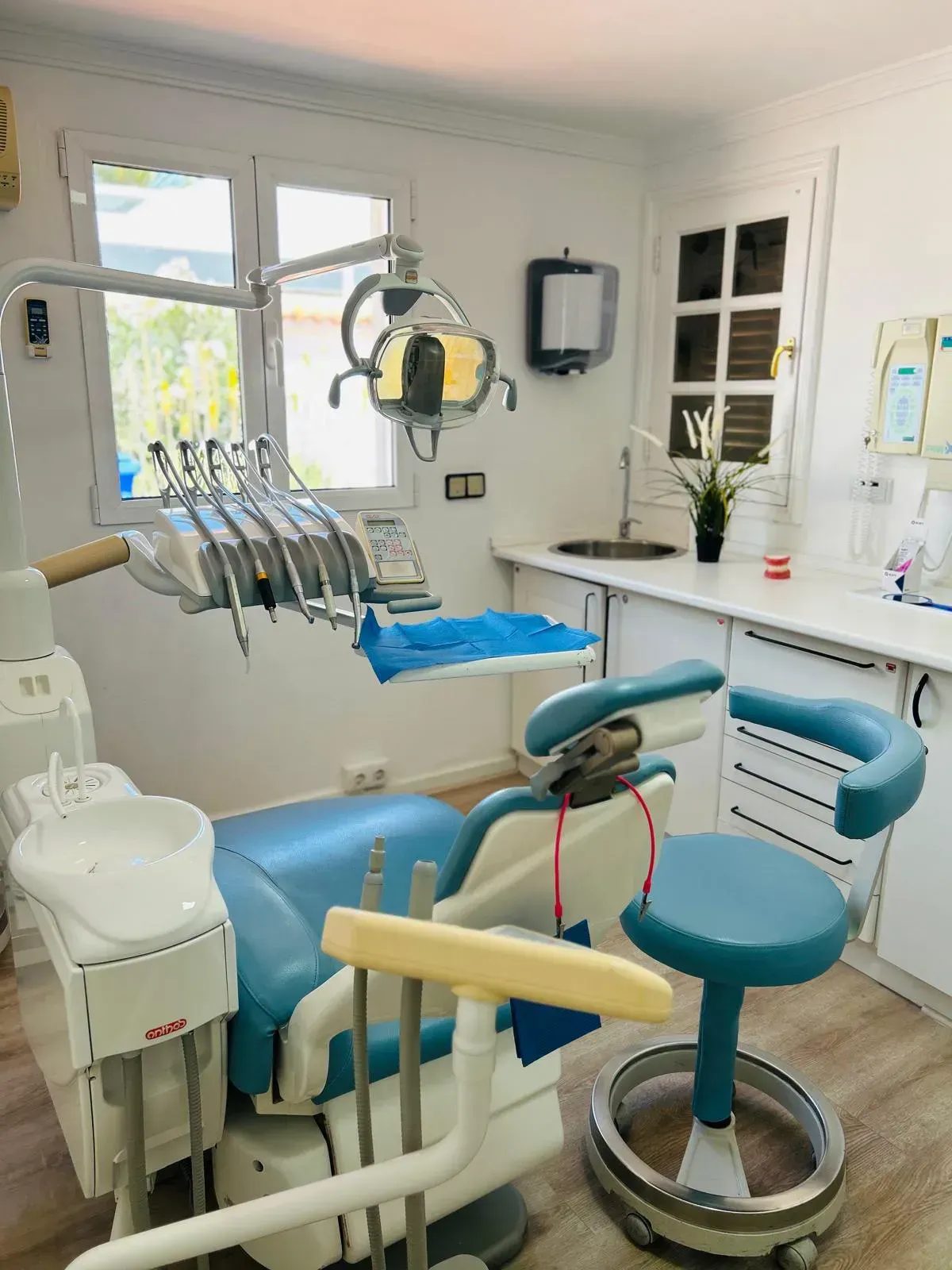 Una sala de tratamiento dental luminosa y limpia, equipada con un sillón azul para el paciente, instrumental dental