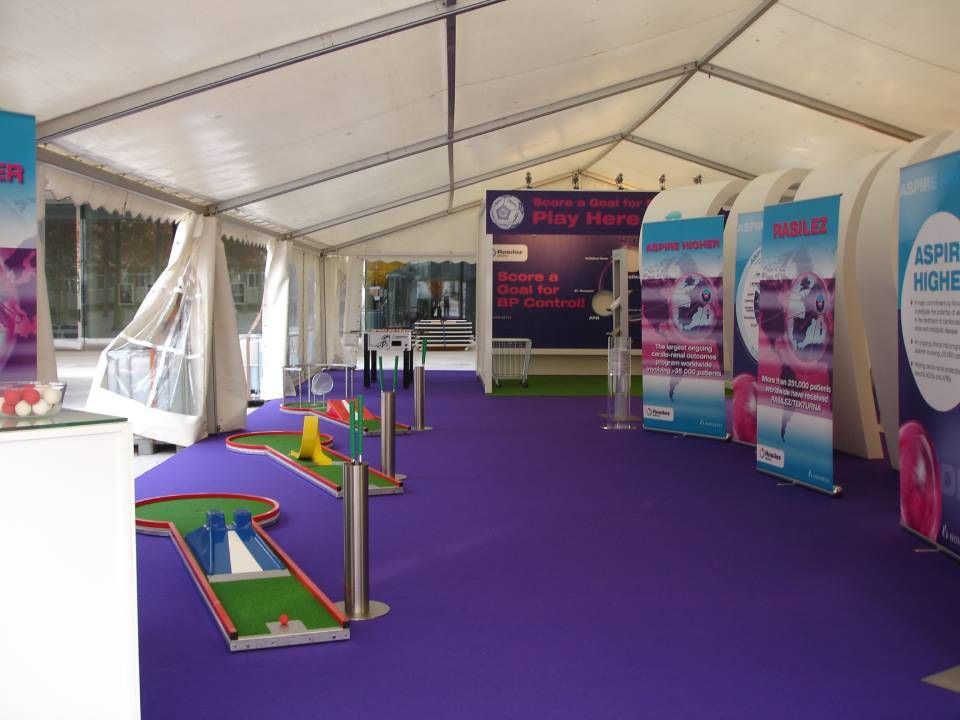 Indoor-Minigolfstand mit lila Teppich, Putt-Putt-Bahnen und Werbebannern unter einem weissen Zelt