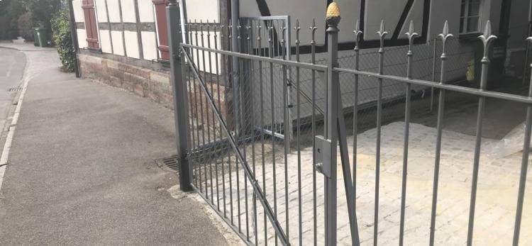 Schwarzer Metallzaun neben einer gepflasterten Straße vor einem Gebäude mit dunklen Türen und Fenstern