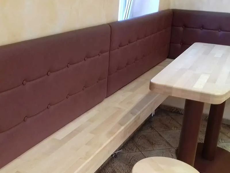Sitznischen aus Holz mit bordeauxroten Kissen und einem hellen Holztisch in einer Café-Ecke