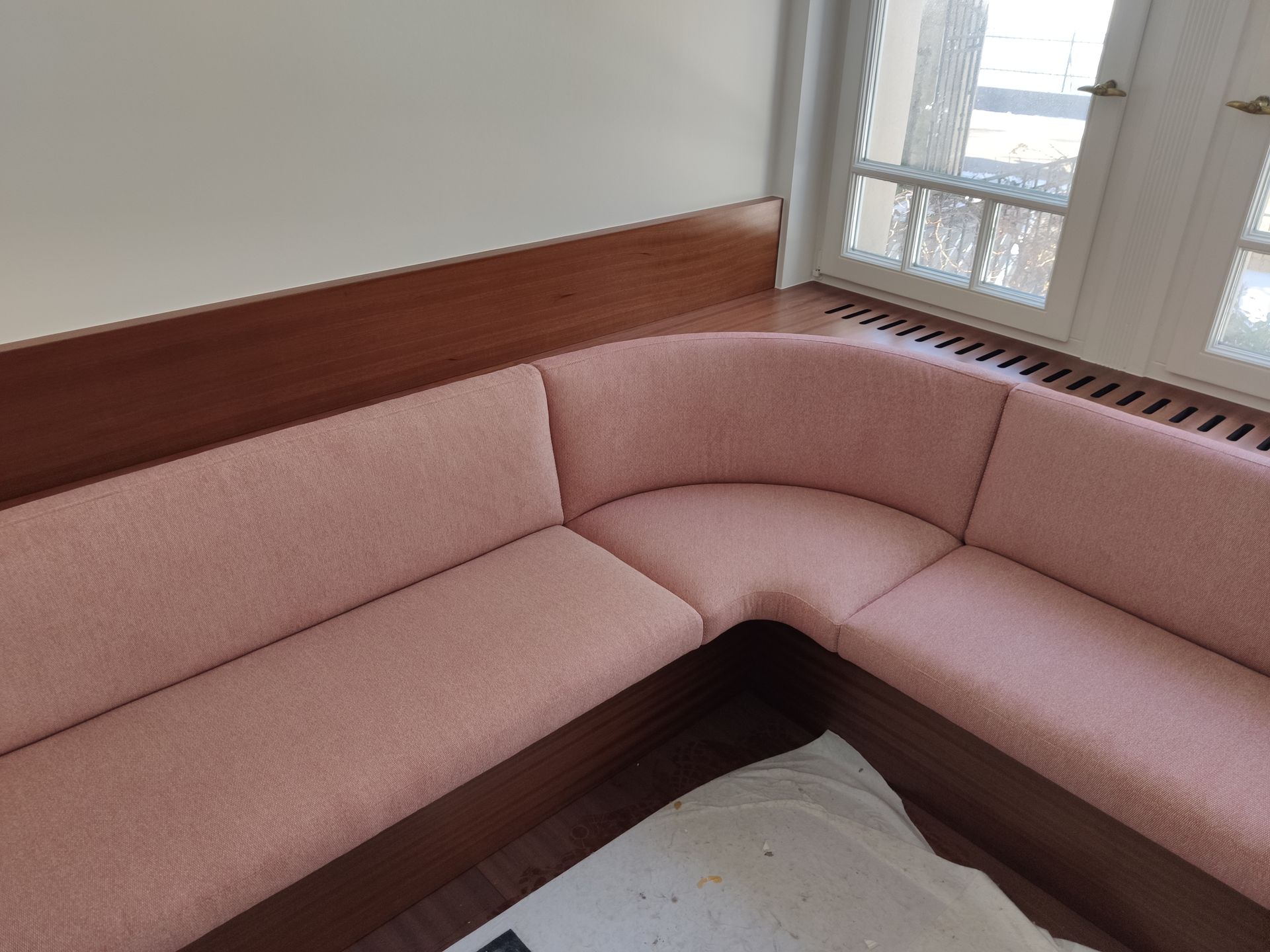 Rosa L-förmiges Ecksofa in einem hellen Zimmer an einem Fenster mit Holzvertäfelung.