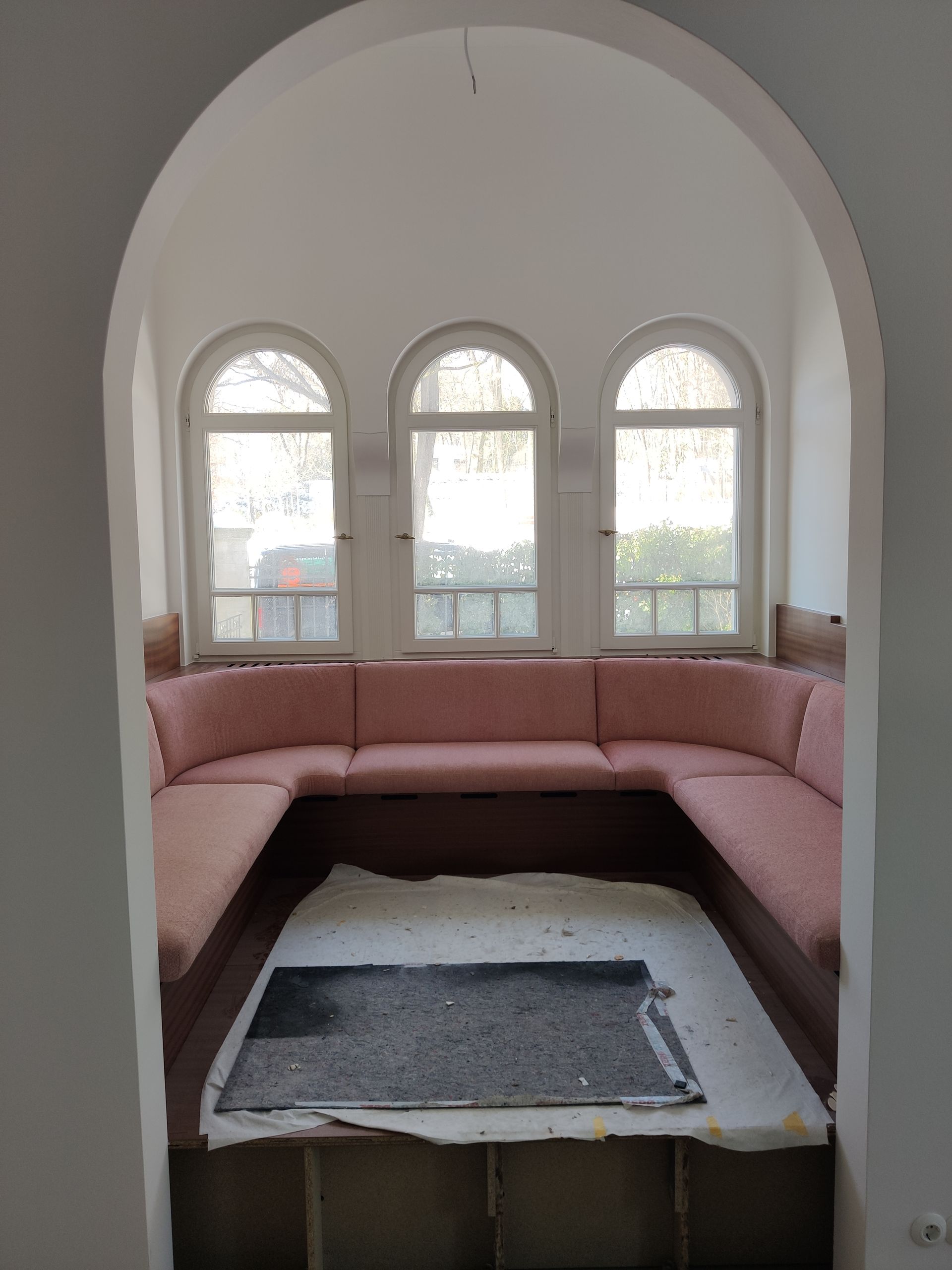 Ein rosafarbener, eingebauter Fenstersitz in einer gewölbten Nische mit drei Fenstern und einem kleinen Tisch.