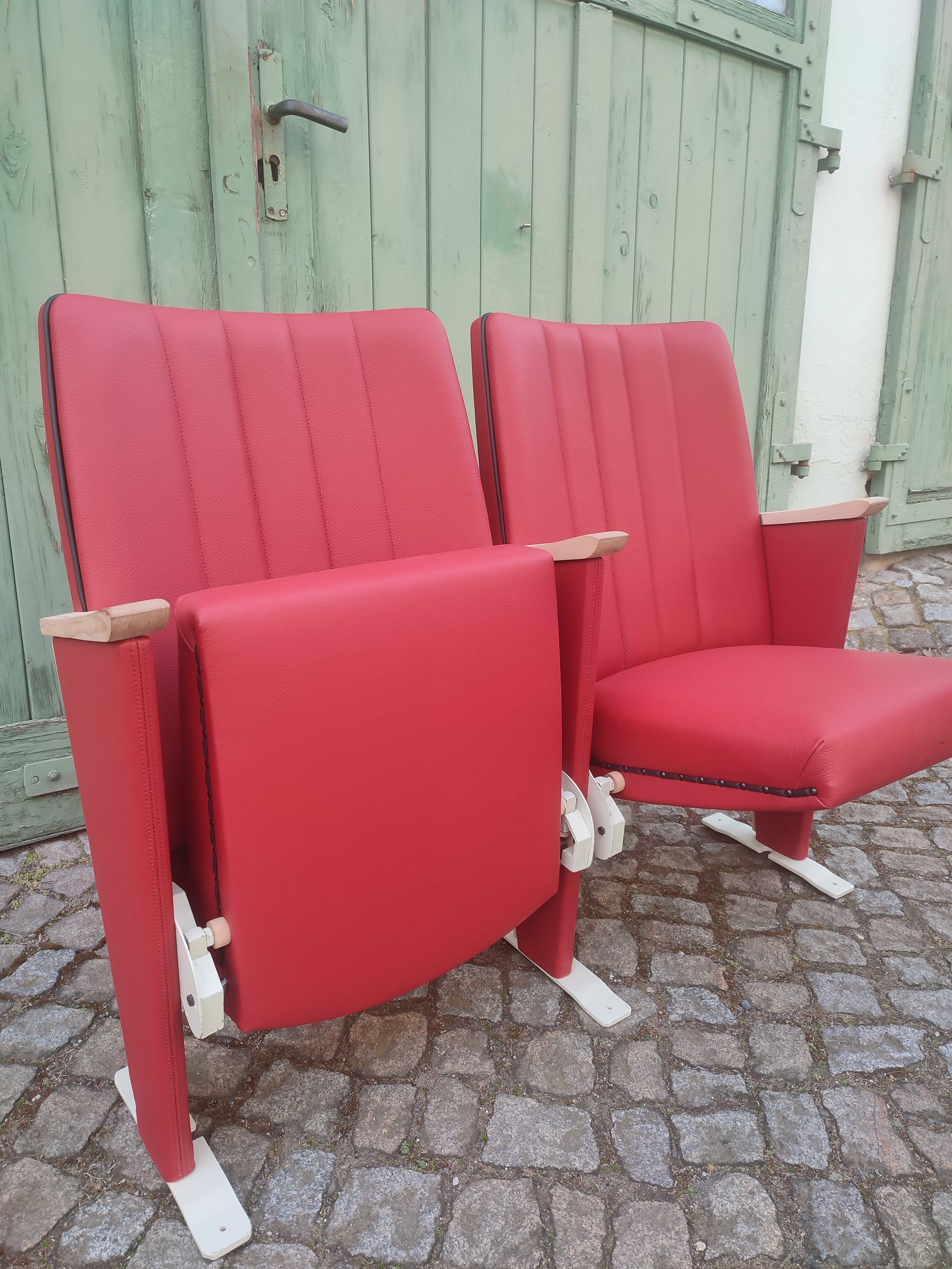 Zwei rote Polsterstühle auf einer gepflasterten Terrasse vor einer grünen Holztür