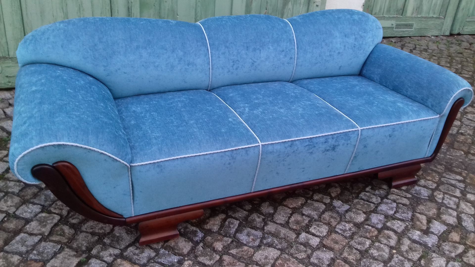 Blaues Polstersofa mit Armlehnen aus Holz auf Kopfsteinpflasteroberfläche