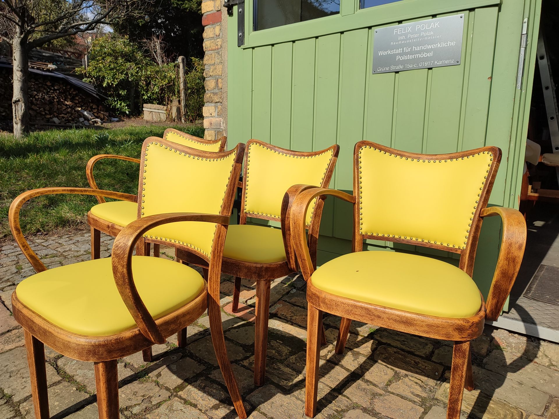 Drei gelbe, gepolsterte Gartenstühle und ein passender Tisch auf einer sonnigen Terrasse neben einer grünen Wand