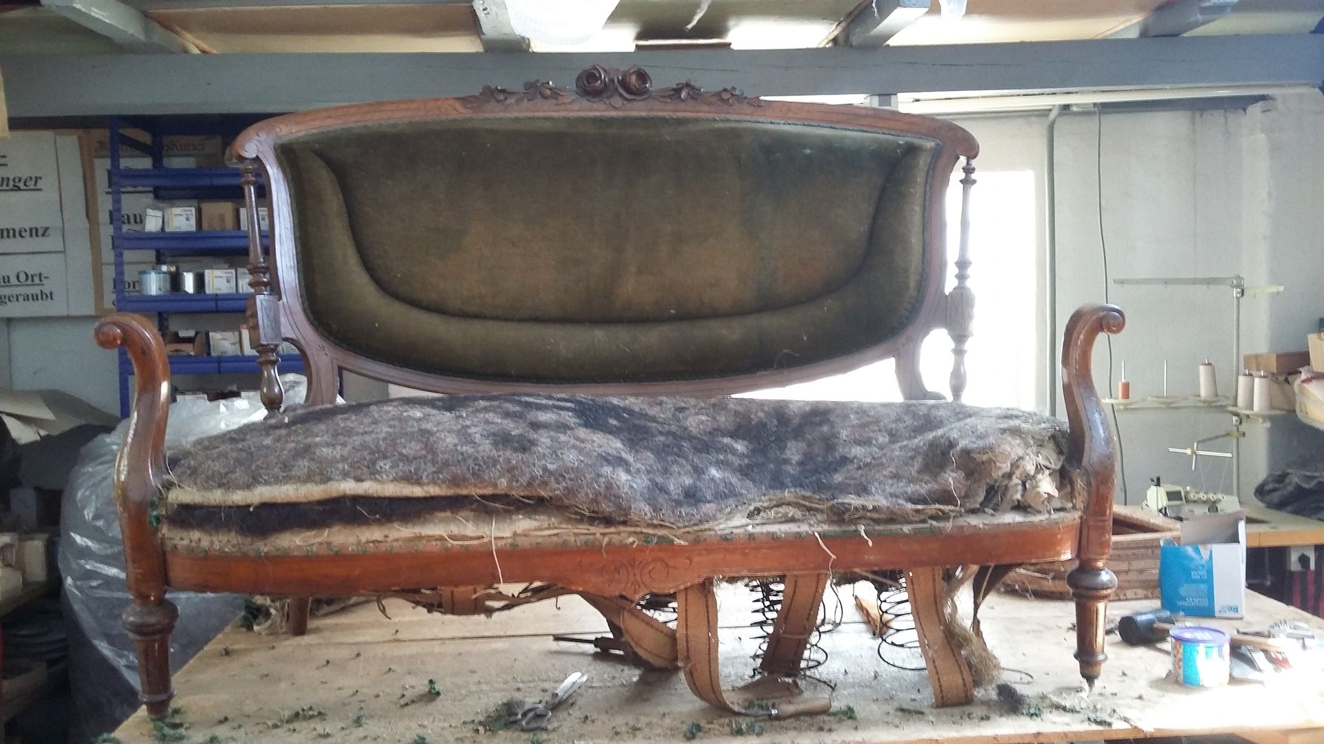 Altes, abgenutztes Sofa mit fleckigen Kissen in einer vollgestellten Garage oder Werkstatt