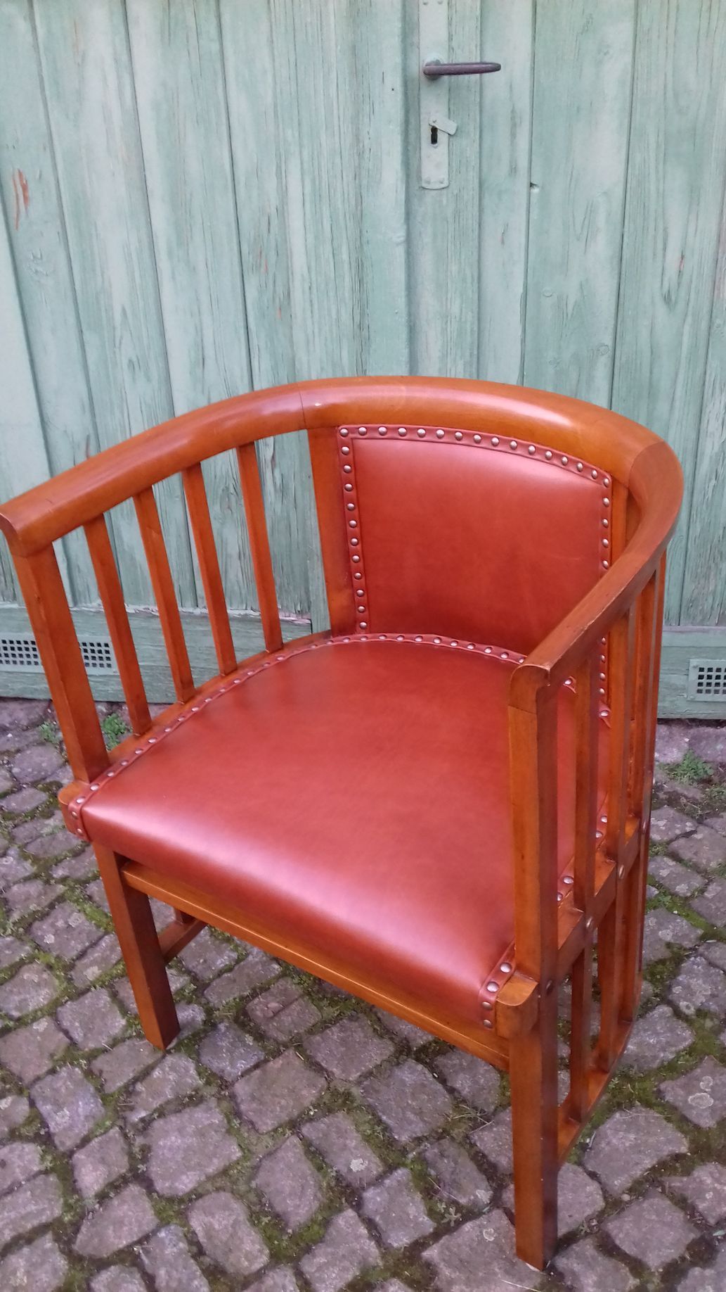 Ein roter Ledersessel mit Holzgestell steht auf einer gepflasterten Terrasse vor einer hellgrünen Tür.