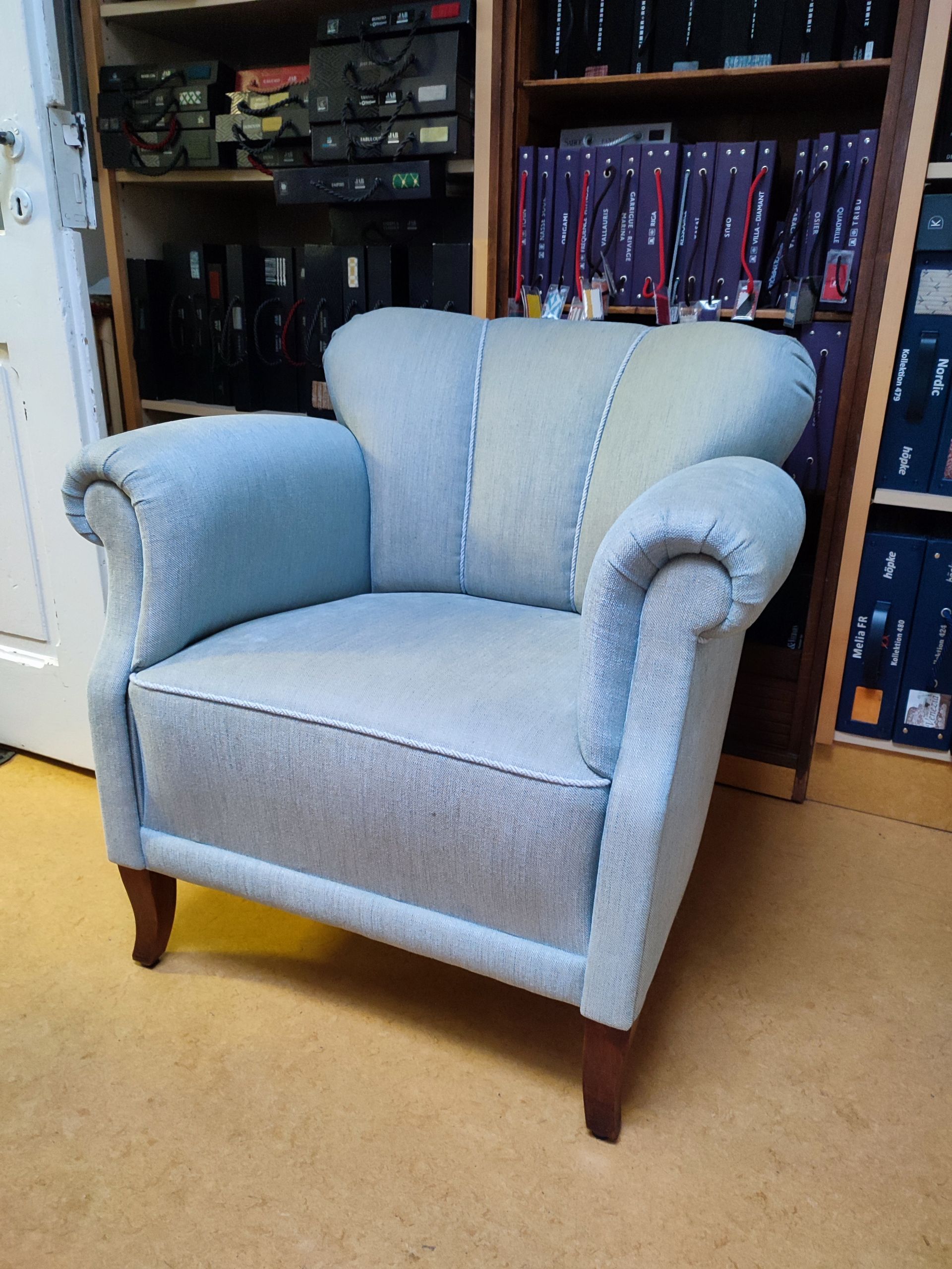 Hellblauer Sessel mit Holzbeinen in einem Zimmer neben Bücherregalen