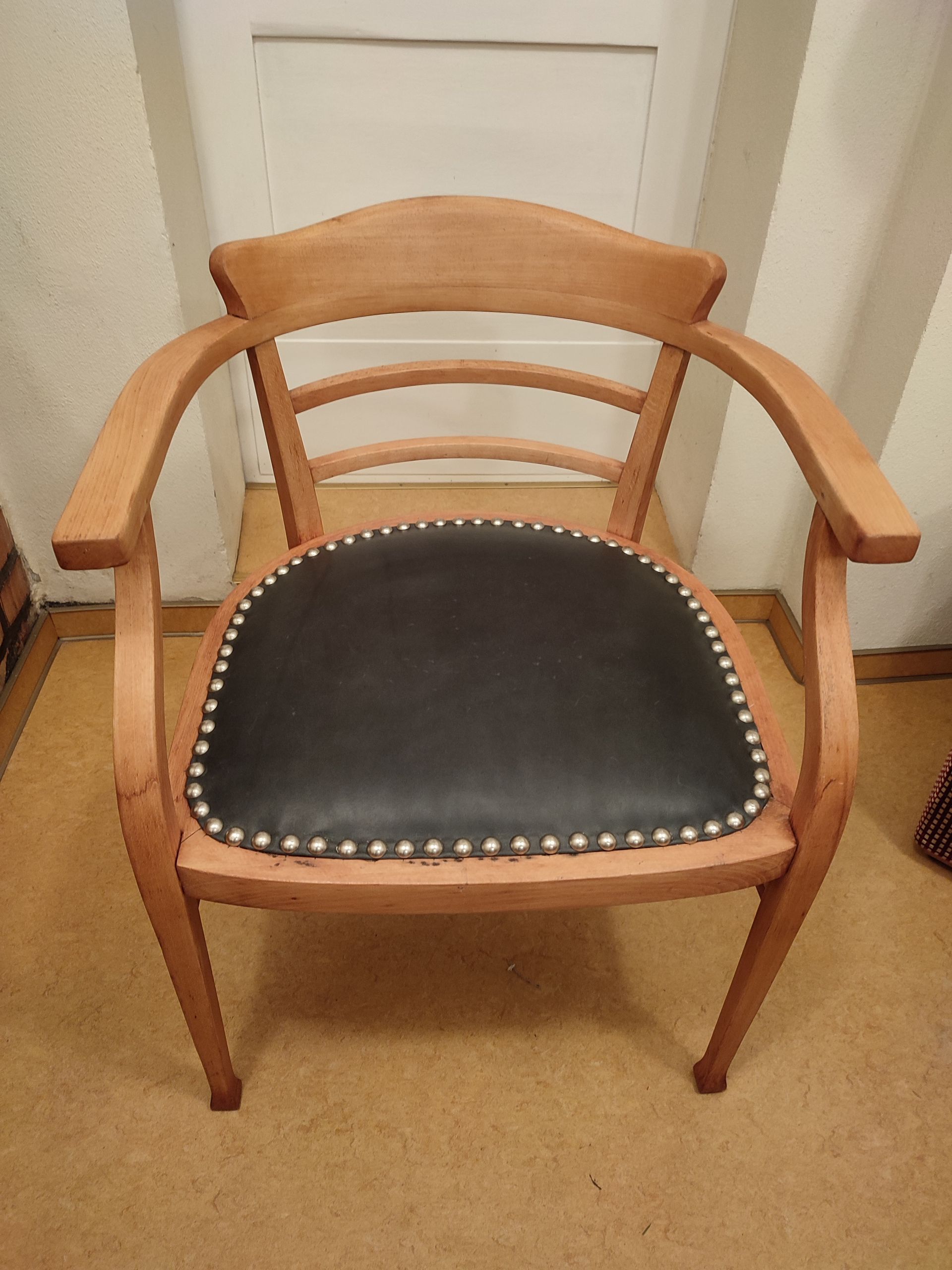 Holzsessel mit schwarzem Sitzkissen in einem beigen Zimmer.