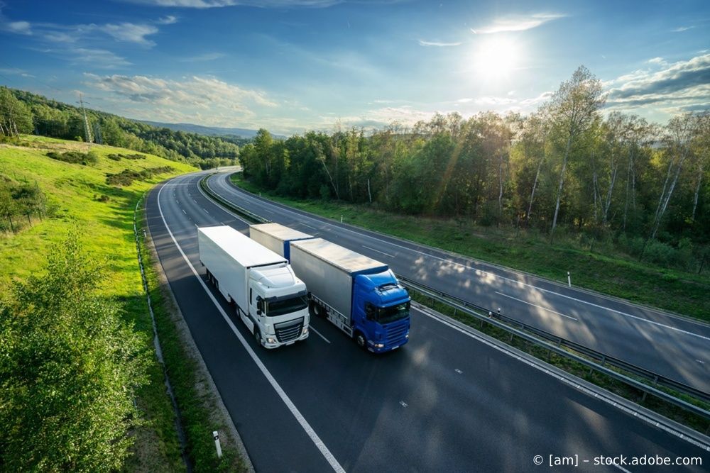 Zwei Sattelschlepper fahren auf einer kurvenreichen Autobahn durch grüne Landschaft unter strahlend blauem Himmel