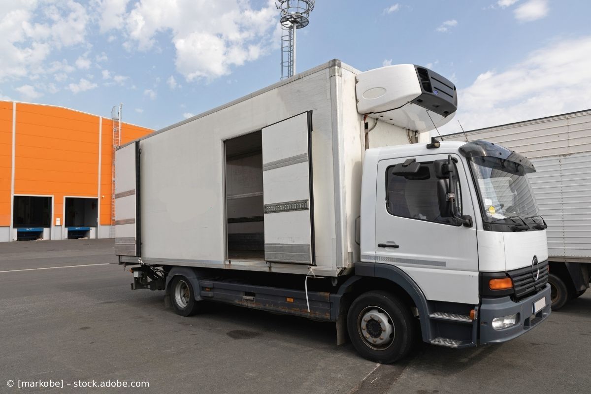 Ein weißer Kastenwagen parkt vor einem Lagerhaus mit orangefarbenen und grauen Gebäuden.