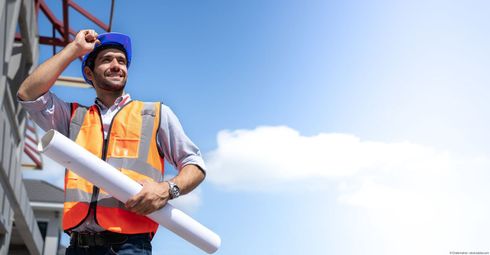 Ein Bauarbeiter trägt einen blauen Helm und eine orangefarbene Schutzweste Ein Bauarbeiter trägt einen blauen Helm und eine orangefarbene Schutzweste