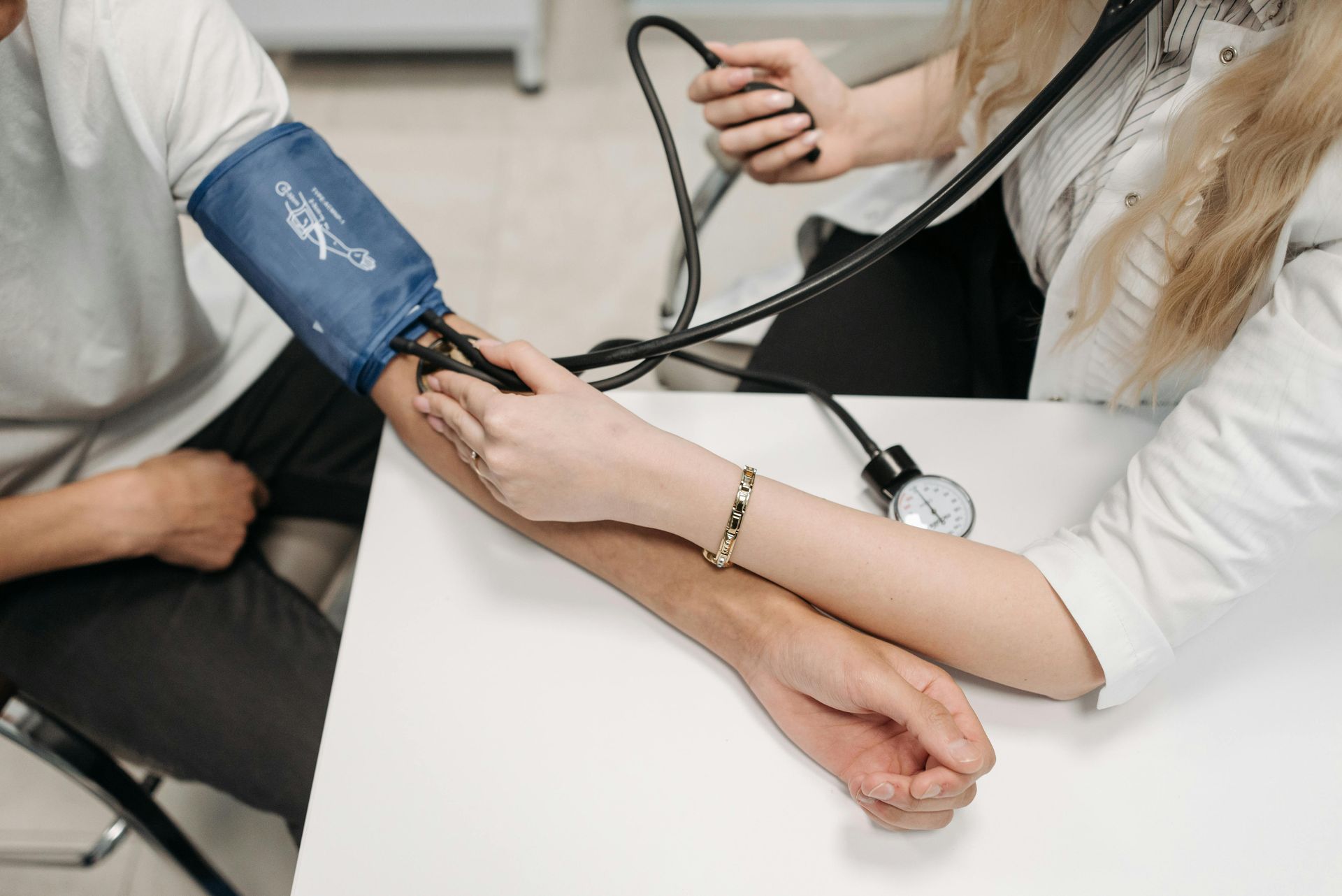 Un profesional sanitario toma la presión arterial de una persona utilizando un brazalete azul y un esfigmomanómetro manual.