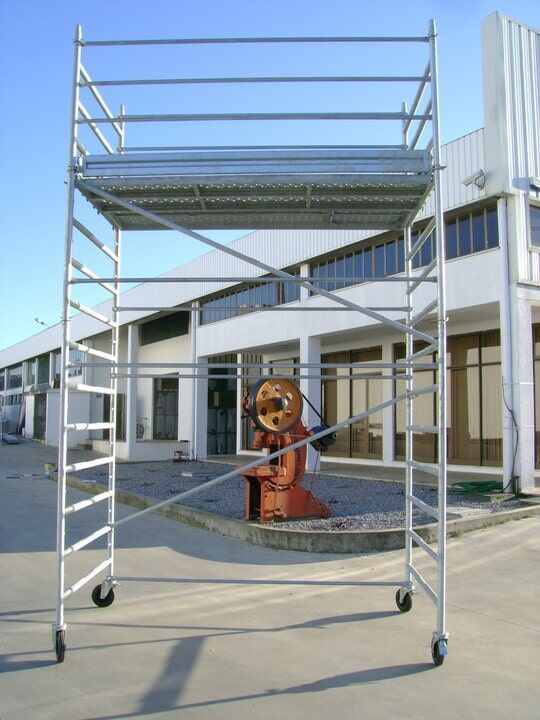 Andaimes sobre rodas, de metal prateado, em frente a um prédio com janelas.