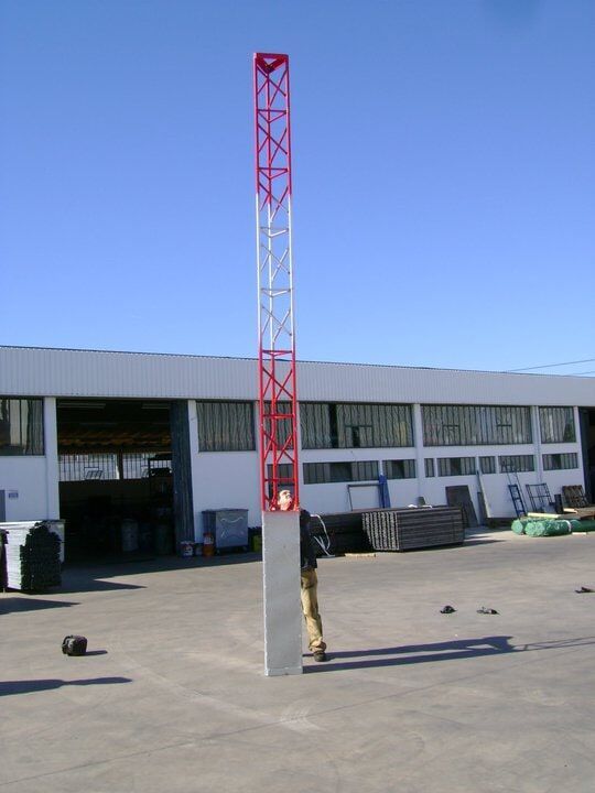 Uma torre alta de metal vermelha e branca com uma pessoa em pé perto de um prédio sob um céu azul.