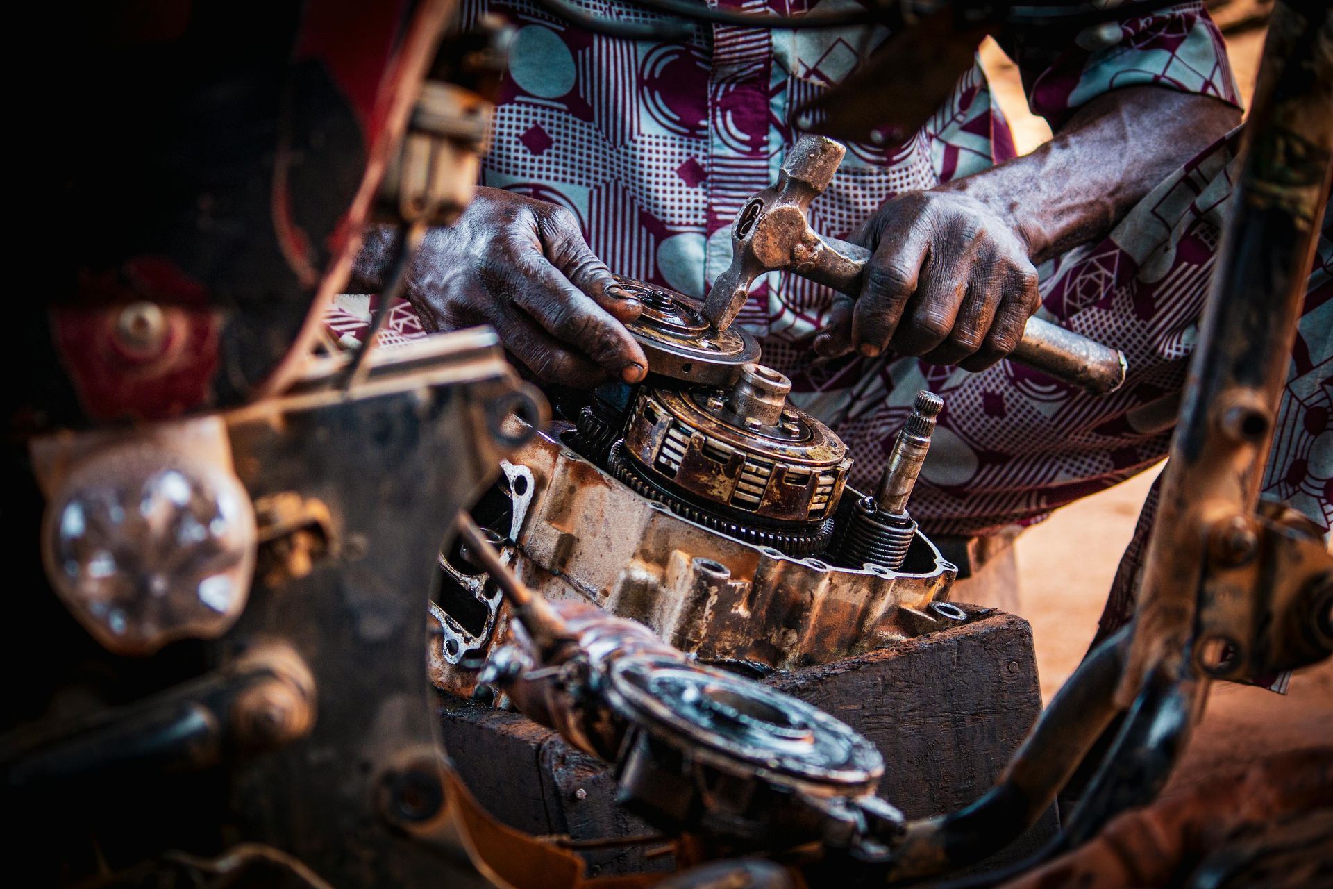 Des mains travaillant sur un moteur mécanique avec des outils, montrant des pièces métalliques graisseuses et des câbles