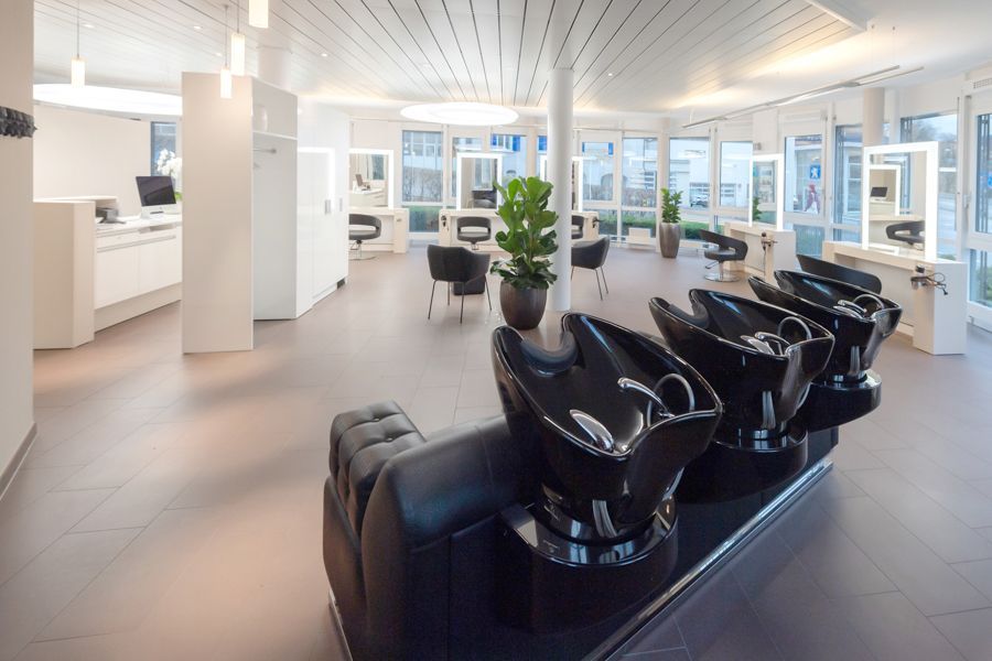Eine Reihe schwarzer Waschbecken in einem großen Raum in einem Friseursalon.