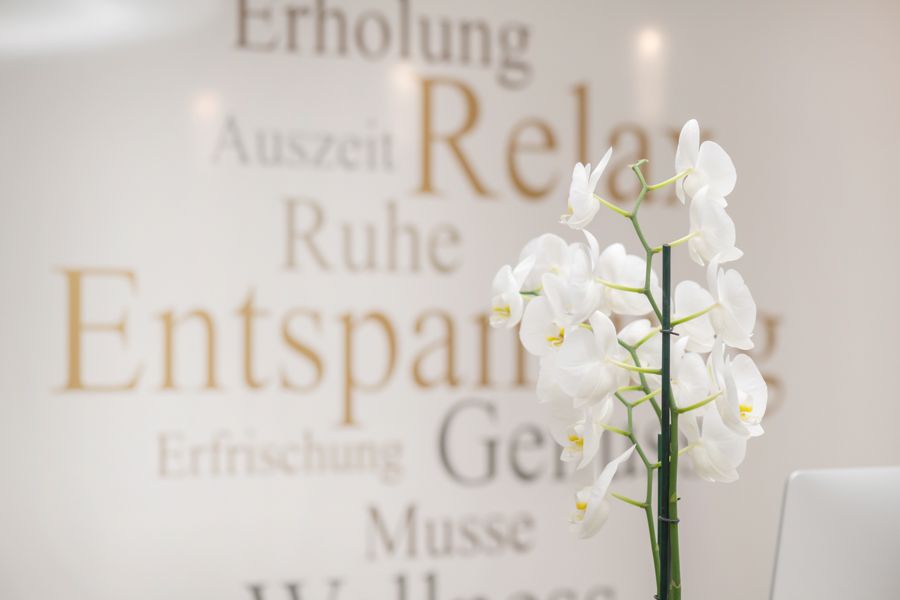 Vor einer Wand steht eine Vase mit weißen Blumen, auf der deutsche Worte stehen.