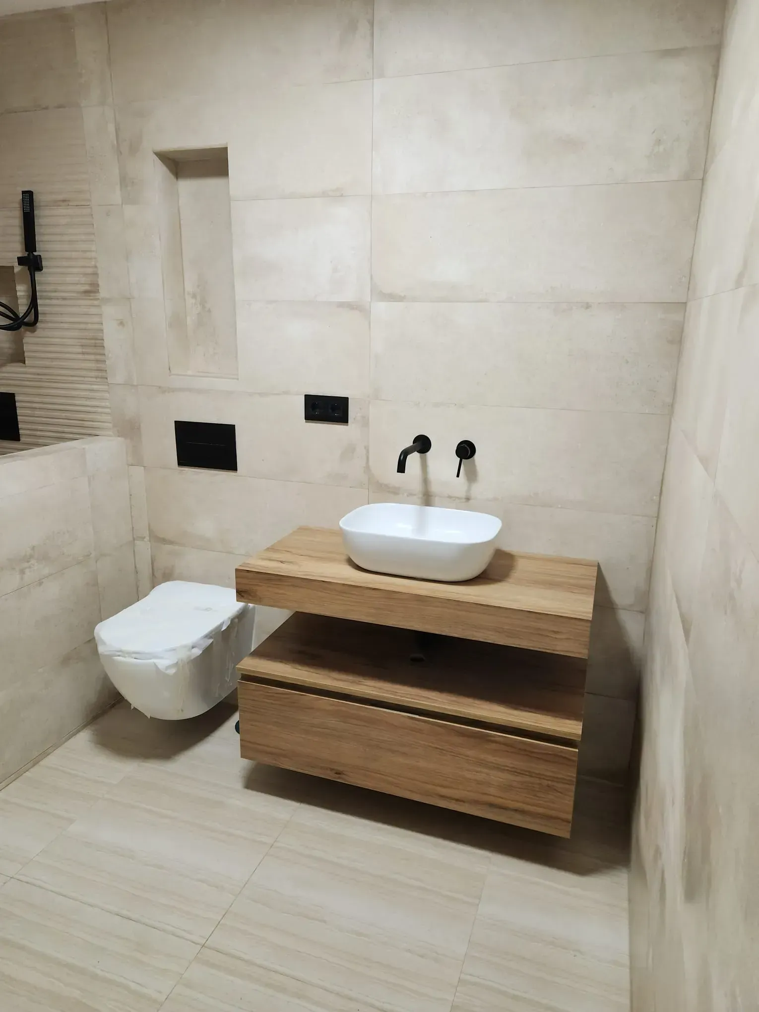 Baño moderno con inodoro suspendido, lavabo sobre mueble de madera y paredes alicatadas en color beige.