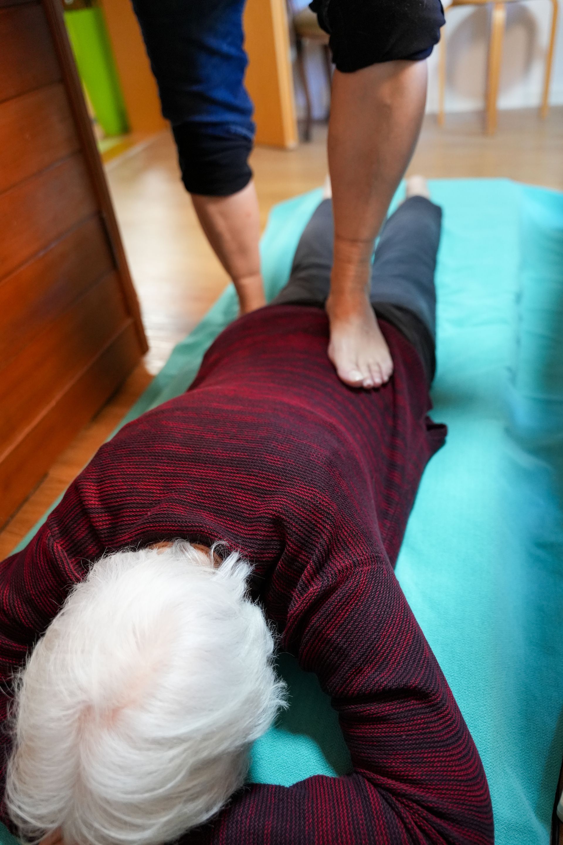 Eine Frau massiert einer liegenden Person den Rücken in einem lichtdurchfluteten Raum.
