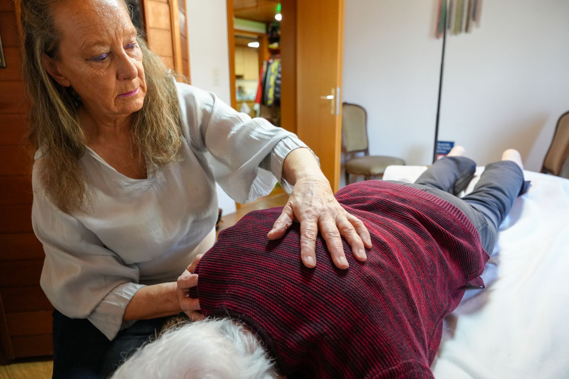 Frau massiert den Rücken; drinnen, Hände auf dem nackten Rücken, konzentrierter Gesichtsausdruck.