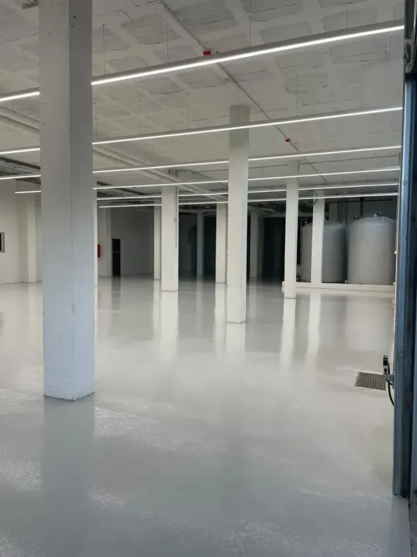 Interior de almacén vacío, espacioso, de paredes blancas, con piso de concreto, pilares.