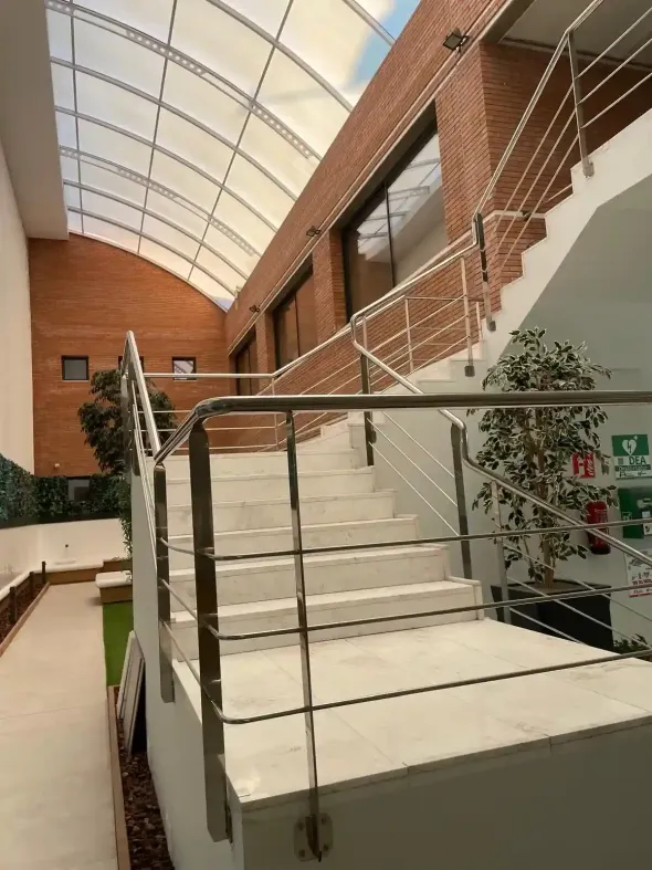 Escalera con barandillas de acero inoxidable, paredes de ladrillo y techo translúcido, que conduce hacia arriba.