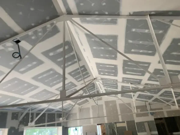 Vista interior de una habitación parcialmente terminada con vigas de techo blancas expuestas.