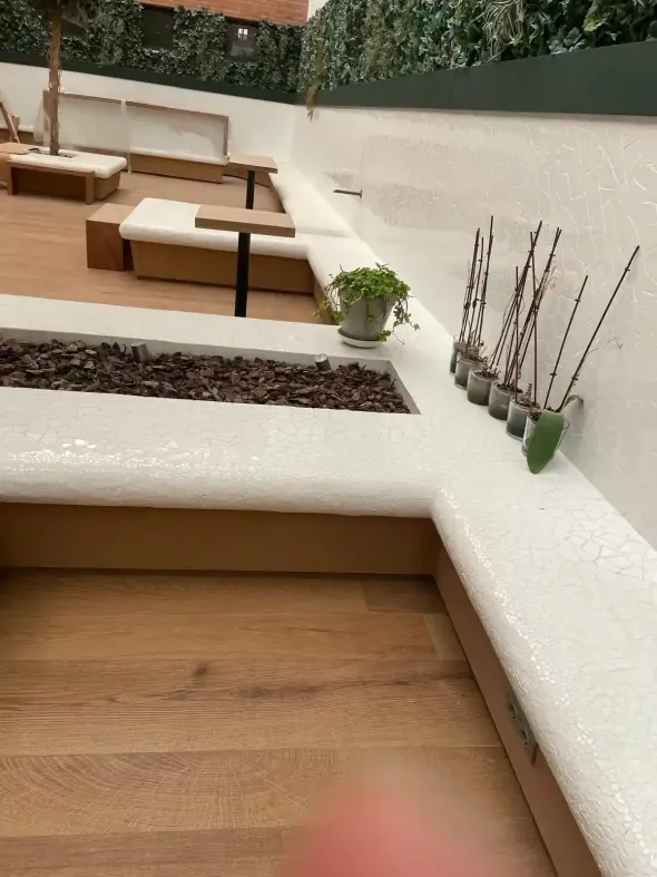 Zona de estar al aire libre con terraza de madera, paredes blancas y pequeñas plantas.