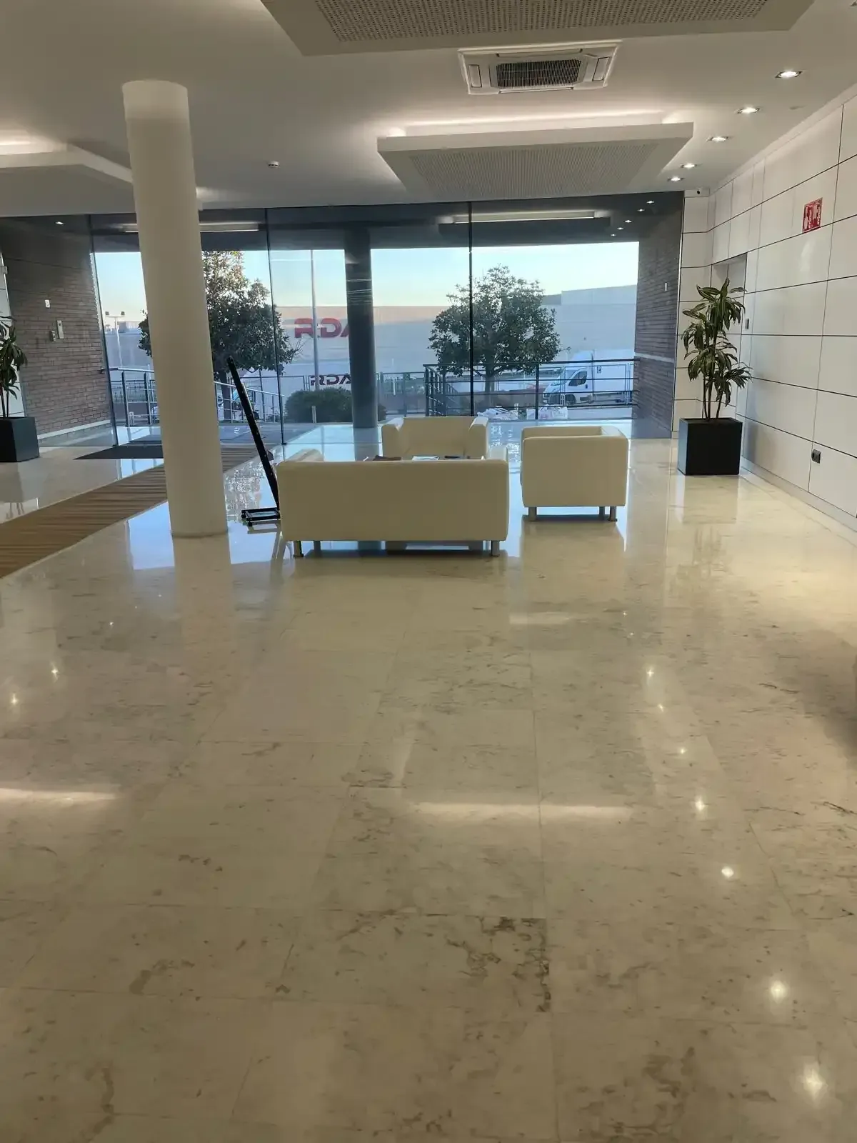 Vestíbulo con suelo de mármol blanco, sofás blancos y grandes ventanales con vistas a la calle.